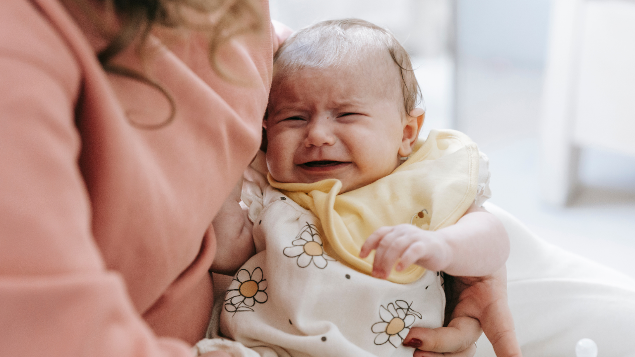mother in pink holds crying infant in yellow bib to illustrate infant reflux in Hudson county